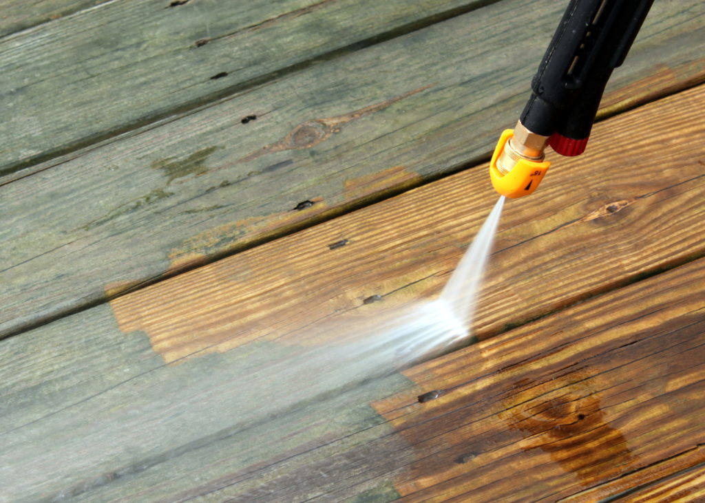 A person using a power washer on wood.